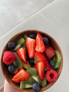 a person holding a wooden bowl filled with fruit