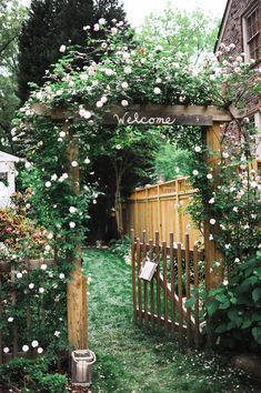 an open wooden gate with white flowers growing on it and welcome sign in the middle