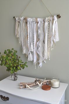 a white dresser topped with a vase filled with flowers and hanging ribbons on the wall