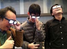 three men wearing glasses looking up at something in the air with their hands on their eyes