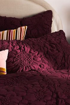 a bed with red comforter and two pillows on top of it, in front of a white headboard