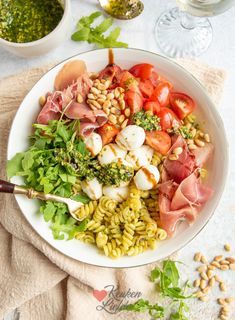 a white bowl filled with lots of food next to two bowls of pesto and pine nuts