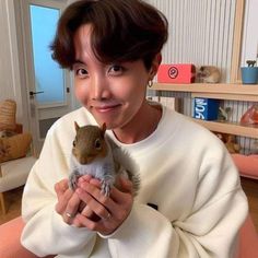 a woman is holding a squirrel in her hands and smiling at the camera while wearing a white sweater