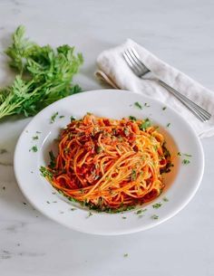 a white plate topped with spaghetti and parsley next to a fork on a table