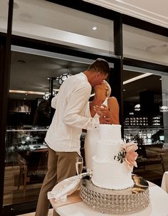 a man and woman kissing in front of a wedding cake