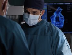 two doctors in scrubs and surgical masks looking at each other with an x - ray behind them