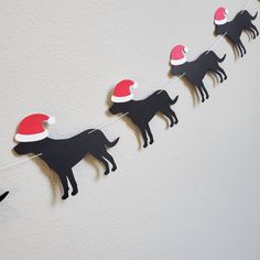 a black dog wearing a santa claus hat is hanging on a string with other dogs