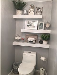 a white toilet sitting in a bathroom next to a shelf filled with pictures and potted plants