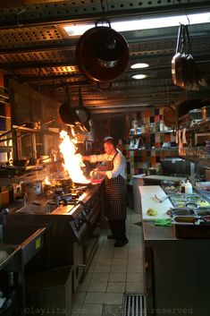 a man cooking in a restaurant kitchen with flames coming out of the pots and pans