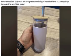 a person holding a cup with a straw in it on top of a wooden table