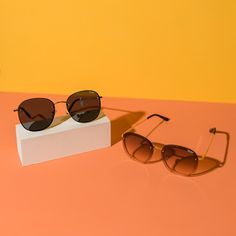 two pairs of sunglasses sitting next to each other on a pink and yellow surface with an orange background