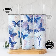 three tumbles with blue butterflies on them are sitting on a wooden stand next to a white wall