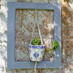 a blue and white potted plant hanging on a stone wall in front of a gray frame