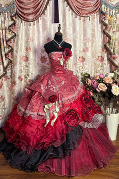 Embrace timeless elegance with this breathtaking quinceanera ball gown, designed for the modern princess with a flair for drama. The strapless bodice features intricate lace appliques and shimmering sequin embellishments, while delicate gold ribbon accents add a regal touch. The voluminous skirt cascades in layers of rich red and black ruffles, adorned with oversized rose appliqués that exude romance and sophistication. A striking blend of classic and gothic aesthetics, this gown is perfect for making a bold and unforgettable entrance on your special day. Fantasy Prom Dress, Red Quince Dress, Quinceanera Rose Gold, Dollcore Outfits, Extravagant Dresses, Black Quinceanera, Ideas Of Outfits, Retro Wedding Dresses