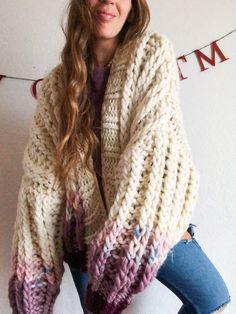 a woman standing in front of a white wall wearing a multicolored knitted sweater