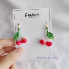 a pair of earrings with cherries hanging from it's earwires in front of a card