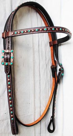 a brown and black horse bridle with turquoise stones on the side, sitting against a white background