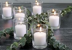 candles are arranged on a table surrounded by greenery and eucalyptus leaves in glass vases