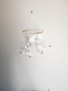 two white birds flying next to each other on a wall with a bird mobile hanging from it's side