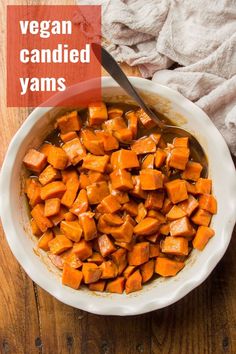 a white bowl filled with sweet potatoes on top of a wooden table next to a spoon