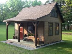 a small wooden building with a porch and covered patio area in the grass next to trees