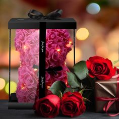 two roses are sitting next to a gift box with a ribbon and lights in the background