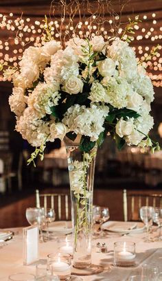 a vase filled with white flowers sitting on top of a table covered in wine glasses