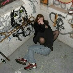 a man sitting on the ground in front of graffiti covered walls