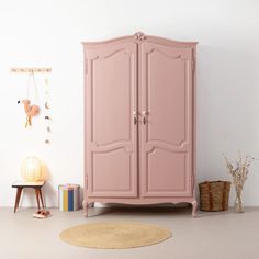 a pink armoire sitting next to a rug on top of a wooden floor in front of a white wall