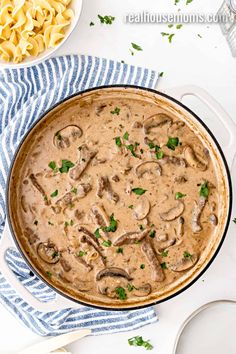 a skillet filled with mushrooms and sauce on top of a blue towel next to pasta