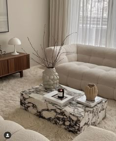 a living room with a couch, coffee table and vase on the floor in front of a window