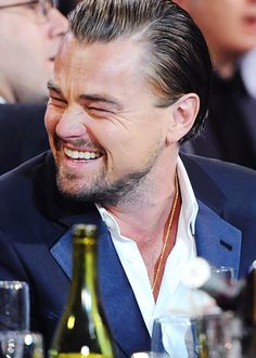 a smiling man sitting at a table with bottles of wine