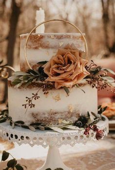 a three tiered cake with flowers and greenery sits on a lace tablecloth