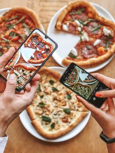 three people taking pictures of pizzas on their phones