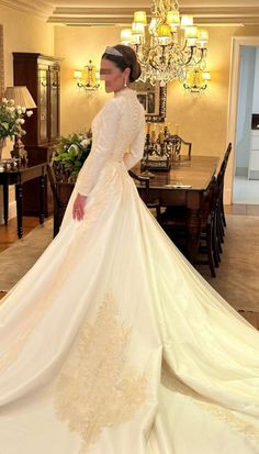 a woman in a white wedding dress is standing near a dining room table and chandelier