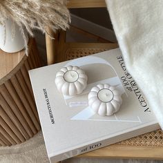 two white ceramic pumpkins sitting on top of a book next to a chair and table