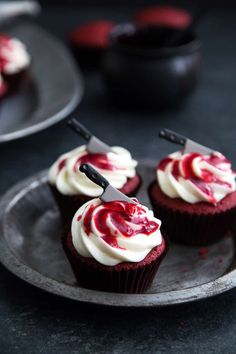 three cupcakes with white frosting and red swirl on top are sitting on a plate