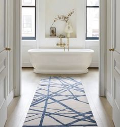 a white bath tub sitting next to two windows in a bathroom on top of a rug