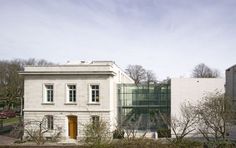 an old white building sitting next to a forest filled with lots of trees and bushes