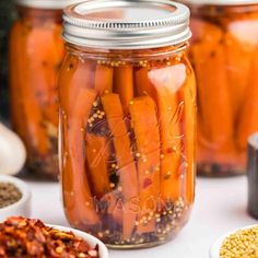 jars filled with carrots sitting on top of a white table next to spices and seasonings