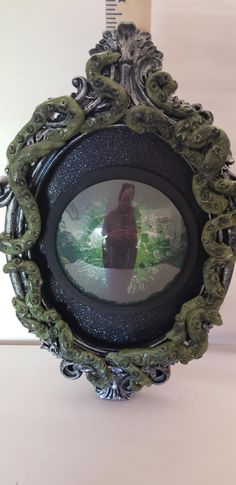 an ornate frame with a bird in the center and green leaves around it on a white surface