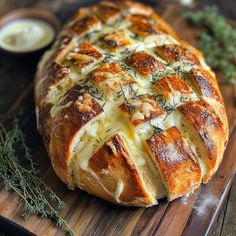 a loaf of bread with cheese and herbs on it sitting on a wooden cutting board