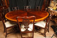 a wooden table with chairs around it in front of a black curtained wall and other antique furniture