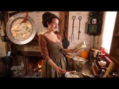 a woman standing in front of a fire holding a book and pot filled with food