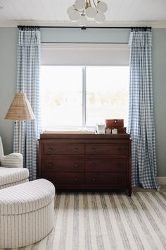 a baby's crib in front of a window with blue and white curtains