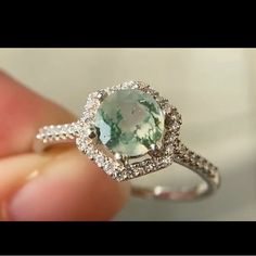 someone is holding an engagement ring with a green stone in it