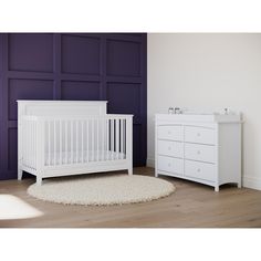 a white crib and dresser in a room with purple walls