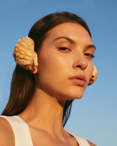 a woman with a seashell in her hair looking off to the side while wearing a white tank top