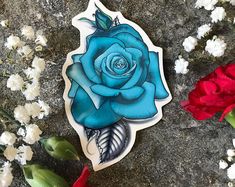 a blue rose sticker sitting on top of a rock next to red and white flowers