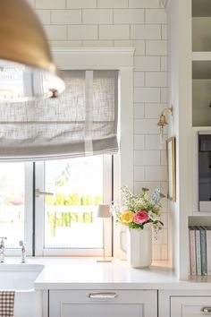 a vase with flowers is sitting on the counter in front of an open kitchen window